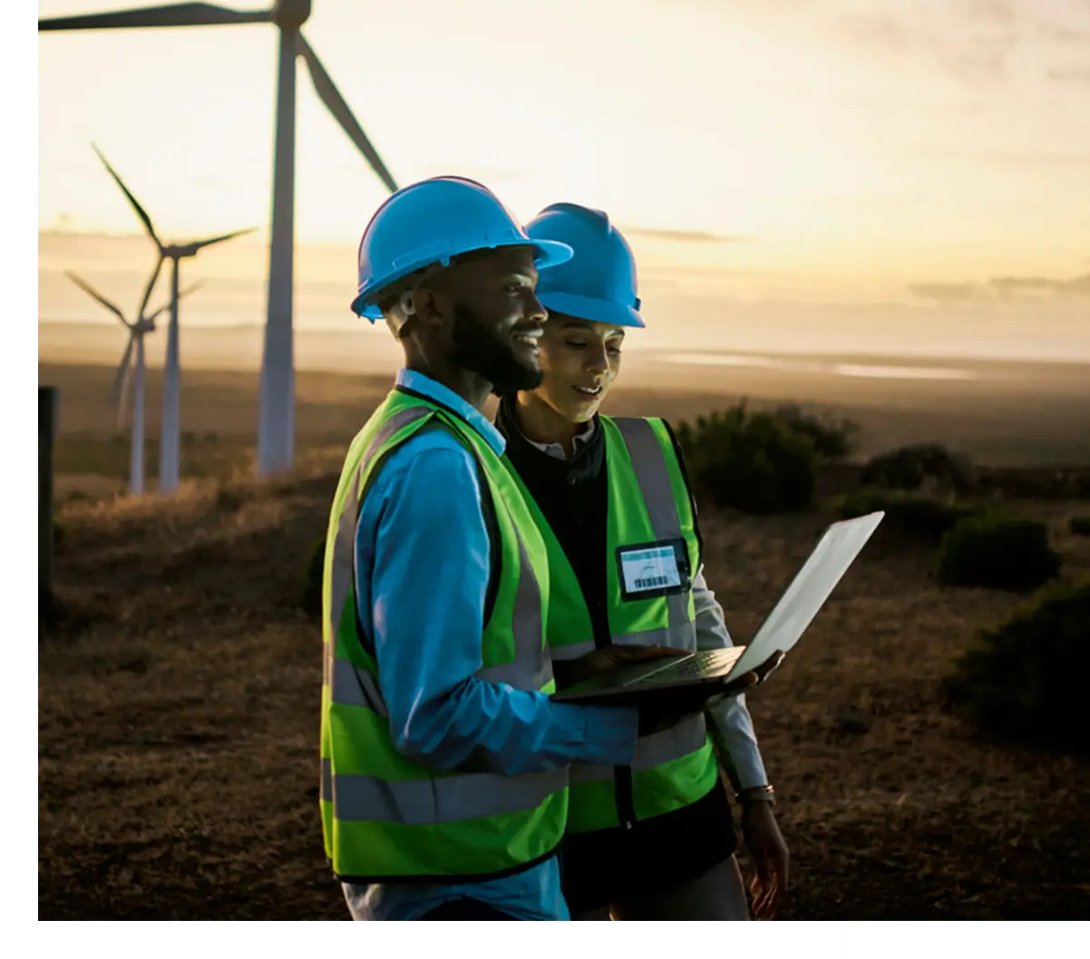 Two field engineers checking laptop by turbines
